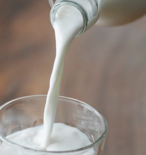 Organic Milk - Crop anonymous person with bottle pouring milk into ornamental transparent glass on wooden table at home