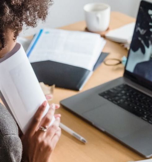 Remote Team - A woman engaged in a virtual meeting at her desk, surrounded by documents and a laptop.