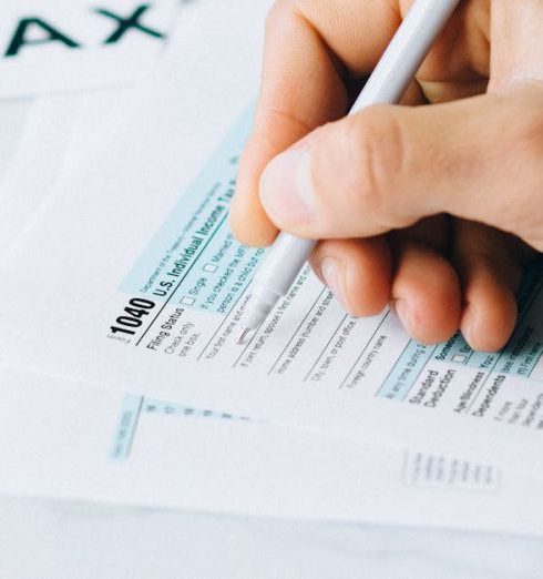 Refunds - Hand completing tax forms with a pen, symbolizing financial deadline and time urgency.