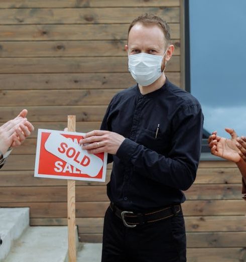 Satisfaction Measurement - Real estate agent and clients celebrate sale with masks and a sold sign outdoors.