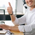 Support Team - Friendly customer service agent wearing headset and smiling with a thumbs up at a modern office desk.