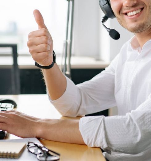 Support Team - Friendly customer service agent wearing headset and smiling with a thumbs up at a modern office desk.