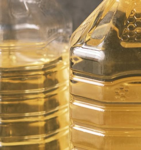 High Volume - Two large recyclable plastic bottles filled with cooking oil on a yellow surface.