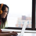 Call Center - Asian woman with headphones using laptop for remote work in a city setting.