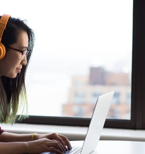 Call Center - Asian woman with headphones using laptop for remote work in a city setting.