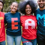 Success Teams - A diverse group of adults bonding and smiling in a park wearing TEAM shirts.