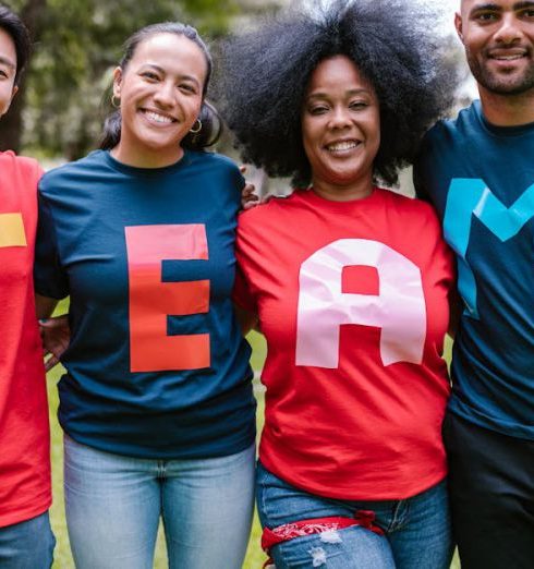 Success Teams - A diverse group of adults bonding and smiling in a park wearing TEAM shirts.