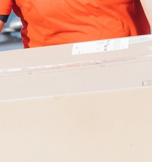 Free Shipping - African American delivery man holding a cardboard box in a residential area, smiling.