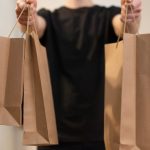 Social Commerce - Adult holding several paper bags representing delivery service indoors.