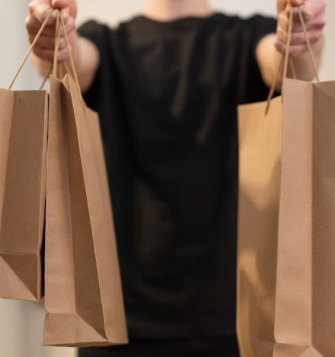 Social Commerce - Adult holding several paper bags representing delivery service indoors.