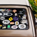 Personalization - A vintage van adorned with various travel stickers parked on an autumn street with colorful foliage.