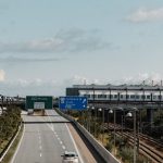 Cross-Border - Aerial view of a highway leading to Sweden from Copenhagen with visible road signs and a train track.