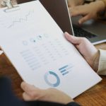 Metrics - Close-up of hands holding a clipboard with charts and graphs in a business meeting.