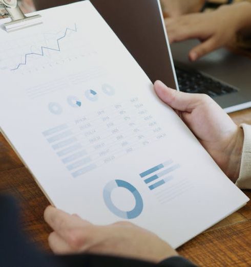 Metrics - Close-up of hands holding a clipboard with charts and graphs in a business meeting.