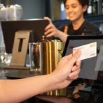 Payment Processing - Person using contactless credit card payment at a modern bar, assisted by a cashier.