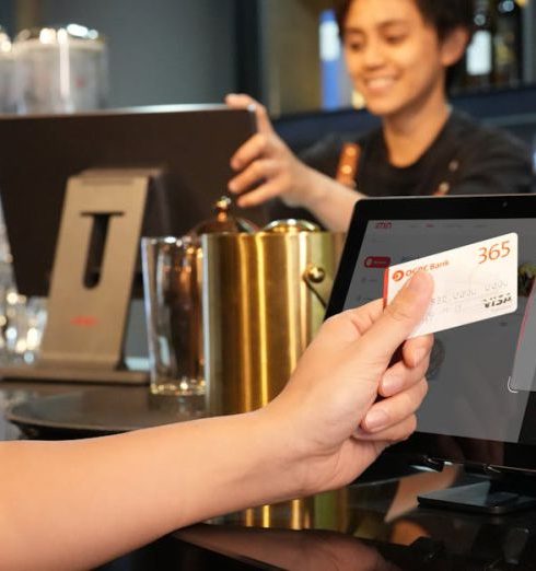 Payment Processing - Person using contactless credit card payment at a modern bar, assisted by a cashier.