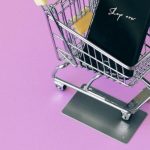 Buy Now Pay Later - Mobile phone in mini cart on pink surface, symbolizing online shopping.