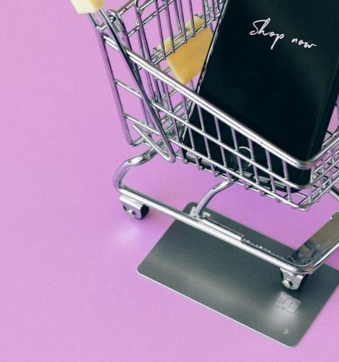 Buy Now Pay Later - Mobile phone in mini cart on pink surface, symbolizing online shopping.