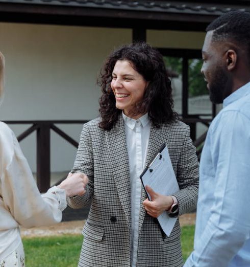 Consultative Selling - A real estate agent shakes hands with a couple outside a modern house, symbolizing a successful property deal.