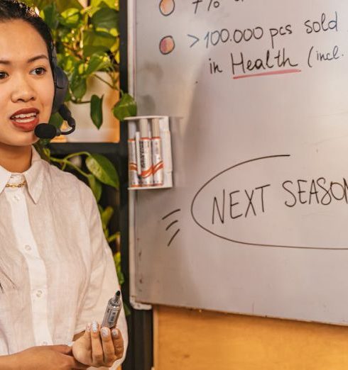 Sales Strategy - Woman presenting business statistics on whiteboard using headset, engaging audience.