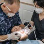 Follow-Up - Dentist and assistant conducting a dental exam with protective gear.