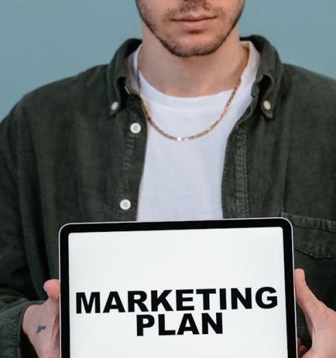 Lead Generation - Adult wearing casual clothing holding a tablet that reads 'Marketing Plan'.