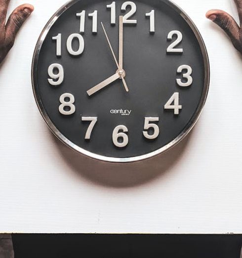 Time Management - High angle view of a man with an apple watch observing a clock on a white table.