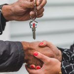 Client Trust - Close-up of a realtor handing over a house key to a new homeowner, symbolizing ownership and investment.