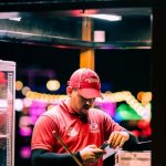 Sales Scripts - A man preparing ice cream cones at a nighttime illuminated booth with colorful lights.