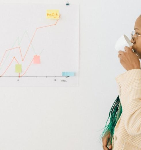 Data Insights - Professional woman in office attire drinking coffee while analyzing a financial graph indoors.