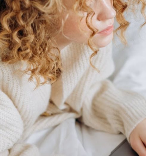 Virtual Meetings - A young woman with curly hair typing on a laptop in bed, epitomizing remote work vibes.