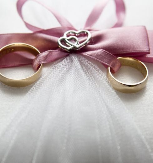 Engagement - Close-up of elegant wedding rings on a silk pillow with a pink ribbon and a heart decoration, symbolizing love.