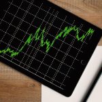 Investment - Flatlay of an iPad displaying stock market graph on a wooden desk with a pencil and paper.