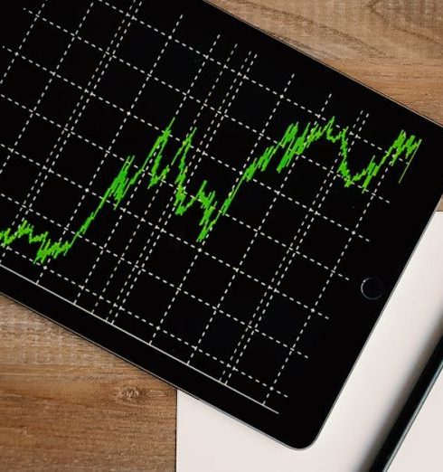 Investment - Flatlay of an iPad displaying stock market graph on a wooden desk with a pencil and paper.