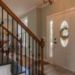 Real Estate - Inviting modern hallway with staircase, chandelier, and natural daylight.