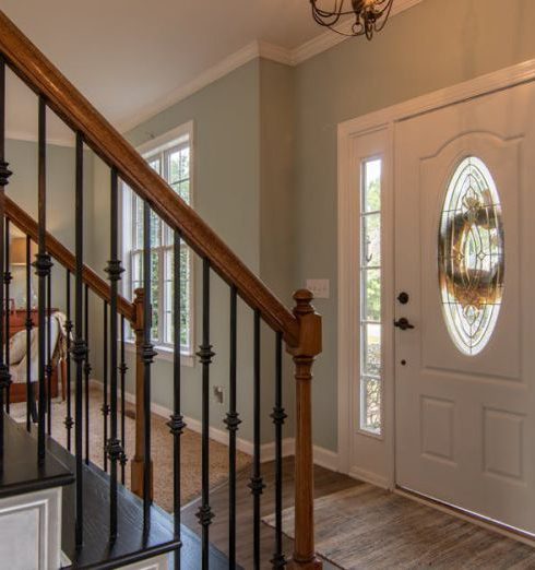 Real Estate - Inviting modern hallway with staircase, chandelier, and natural daylight.