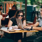 Startups - A group of young adults working on a laptop at an outdoor coffee shop, enjoying teamwork and collaboration.