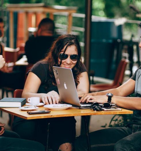 Startups - A group of young adults working on a laptop at an outdoor coffee shop, enjoying teamwork and collaboration.