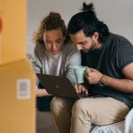 Real Estate Metrics - Couple surrounded by boxes checks laptop details on moving day.