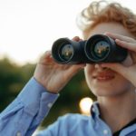 Long-Term Potential - A young person uses binoculars during a nature observation adventure.