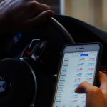 Forex - Person using mobile phone for currency trading while driving BMW car.