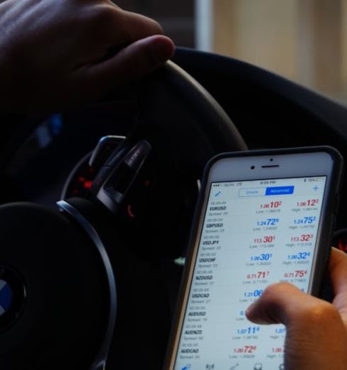 Forex - Person using mobile phone for currency trading while driving BMW car.