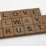 Trusts - Close-up of wooden Scrabble tiles spelling 'Love Always Trusts' on white surface.