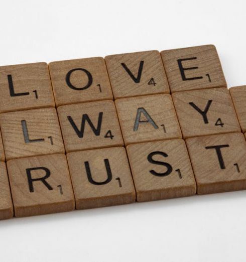 Trusts - Close-up of wooden Scrabble tiles spelling 'Love Always Trusts' on white surface.