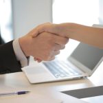 Hiring - Close-up of a professional handshake over a laptop during a business meeting in an office.