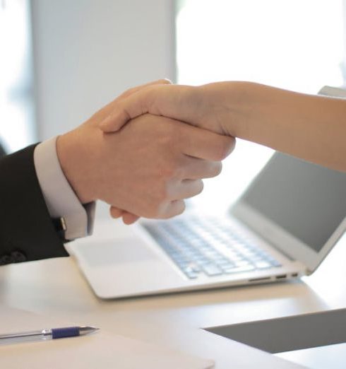 Hiring - Close-up of a professional handshake over a laptop during a business meeting in an office.