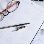 Performance Reviews - Overhead view of a desk with glasses, a pen, calendar, and tax documents.