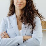 Company Culture - Professional woman in a white blazer standing confidently in an office with arms crossed.