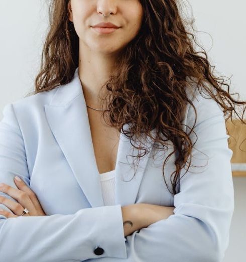 Company Culture - Professional woman in a white blazer standing confidently in an office with arms crossed.