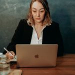 Employee Handbook - A focused businesswoman working on a laptop in a stylish office setting. Professional and determined demeanor.